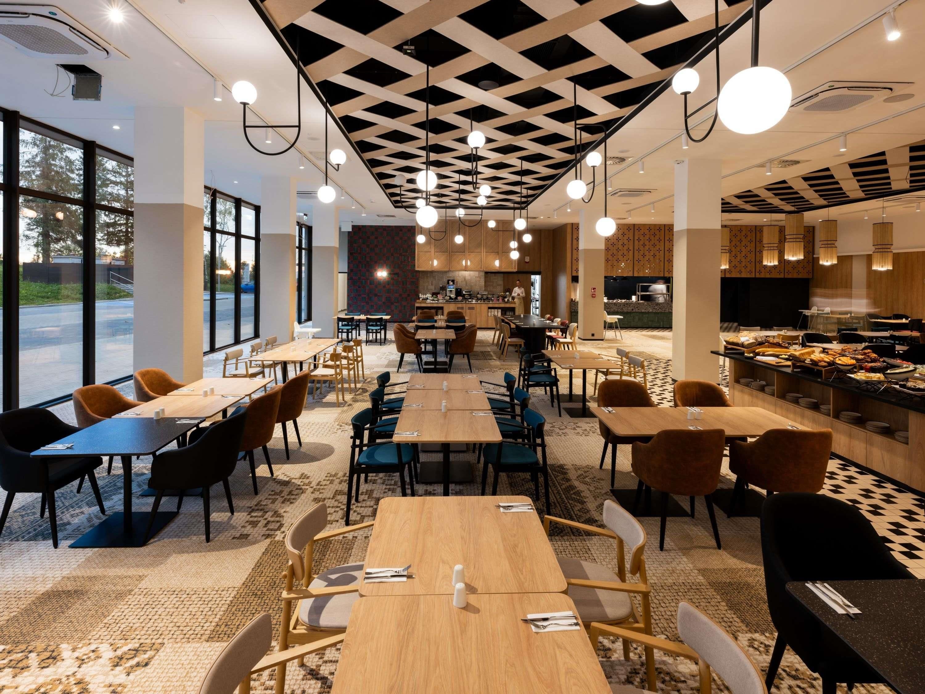 Ein modernes Restaurant mit einem zentralen Essbereich, einer Speiseausgabe und einer im Hintergrund erkennbaren Küche.
