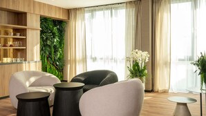Un salon moderne comprenant un canapé, deux petites tables d’appoint rondes, une table basse et une grande fenêtre avec des rideaux.
