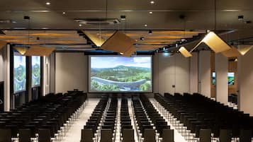 A conference room with rows of chairs, a large screen displaying a hotel, and a modern ceiling design.