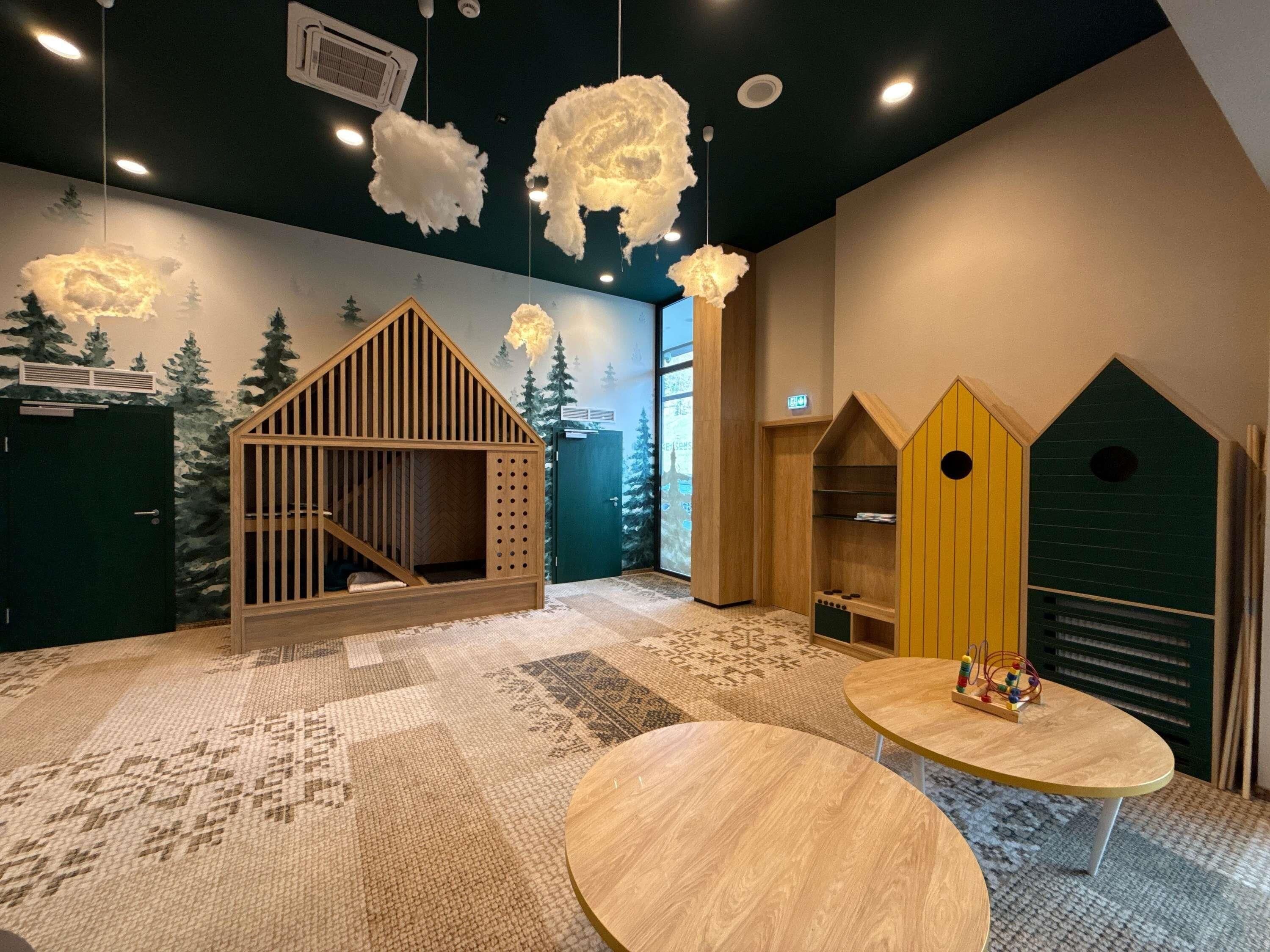 A children's play area with a wooden house, a yellow playhouse, and a patterned carpet.