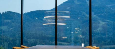 Una mesa de madera con una lámpara colgante moderna, ventanas amplias con vistas a la montaña.