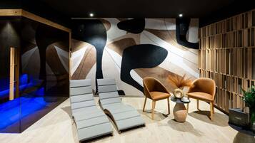 A modern spa room with a geometric wall design, a seating area with two chairs, and a massage table.