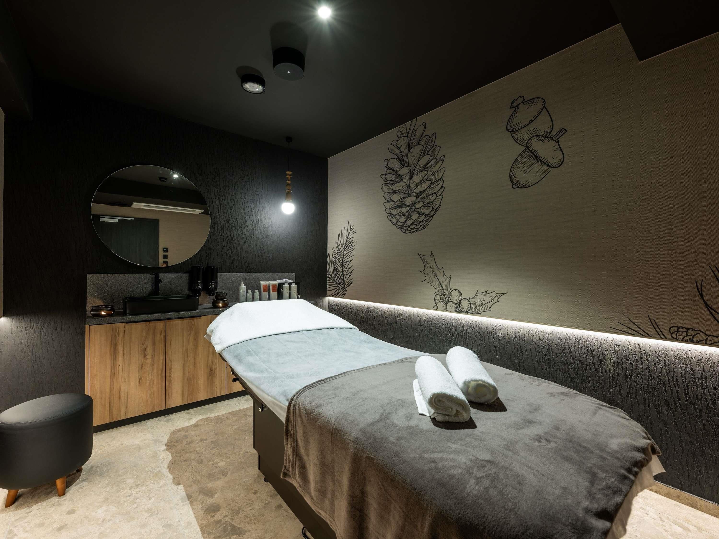 Une salle de spa équipée d’une table de massage, d’un miroir rond, d’armoires en bois et d’œuvres d’art murales.