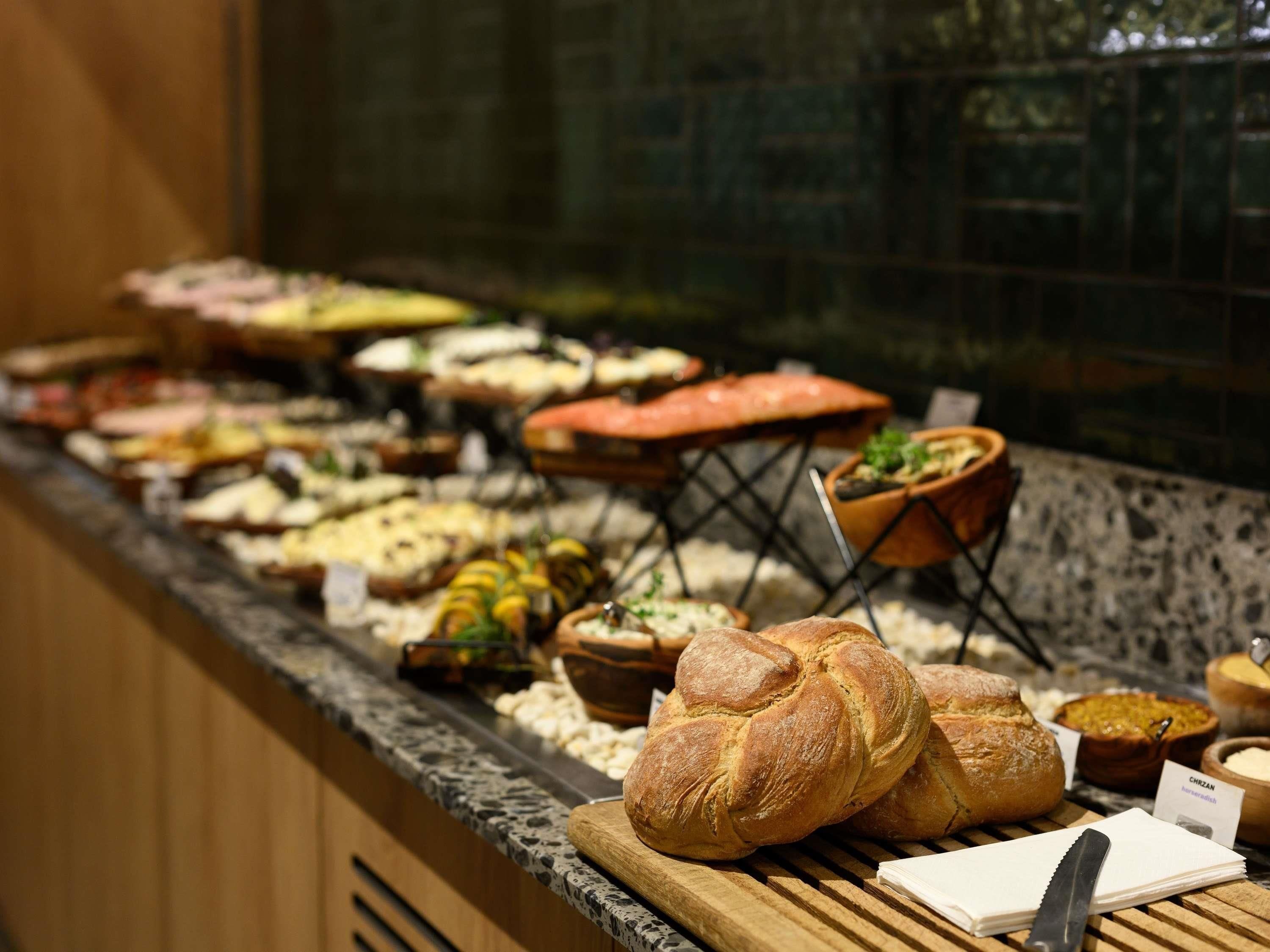 A buffet with various food items and a loaf of bread on a cutting board.