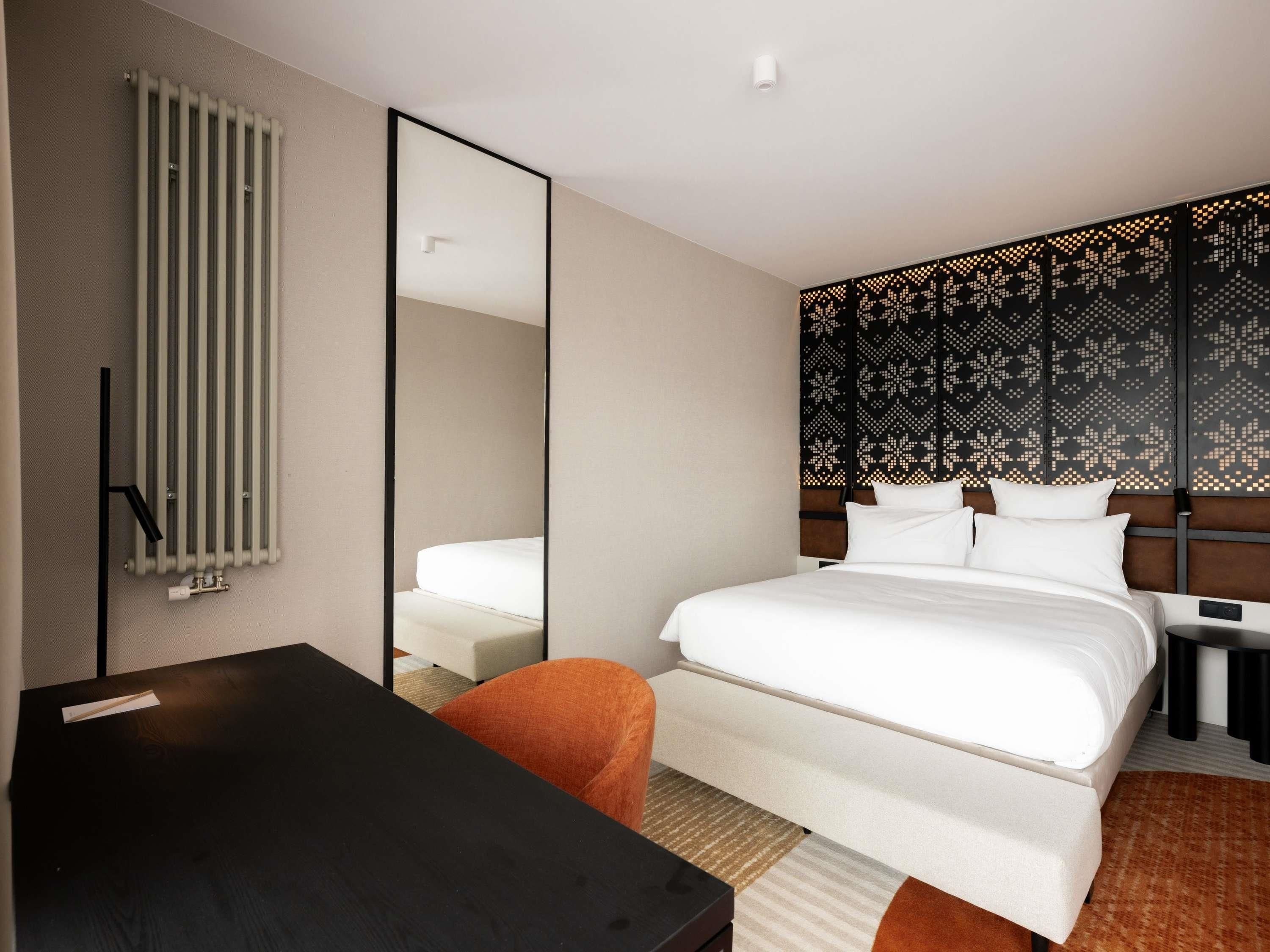 Habitación de hotel con cama, escritorio, silla, espejo, radiador y pared con diseño.