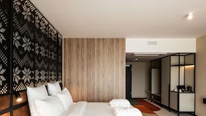 Une chambre d’hôtel moderne avec un grand lit, un mur revêtu de panneaux en bois, un panneau décoratif noir et un petit coin salon.