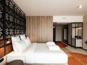 Une chambre d’hôtel moderne avec un grand lit, un mur revêtu de panneaux en bois, un panneau décoratif noir et un petit coin salon.