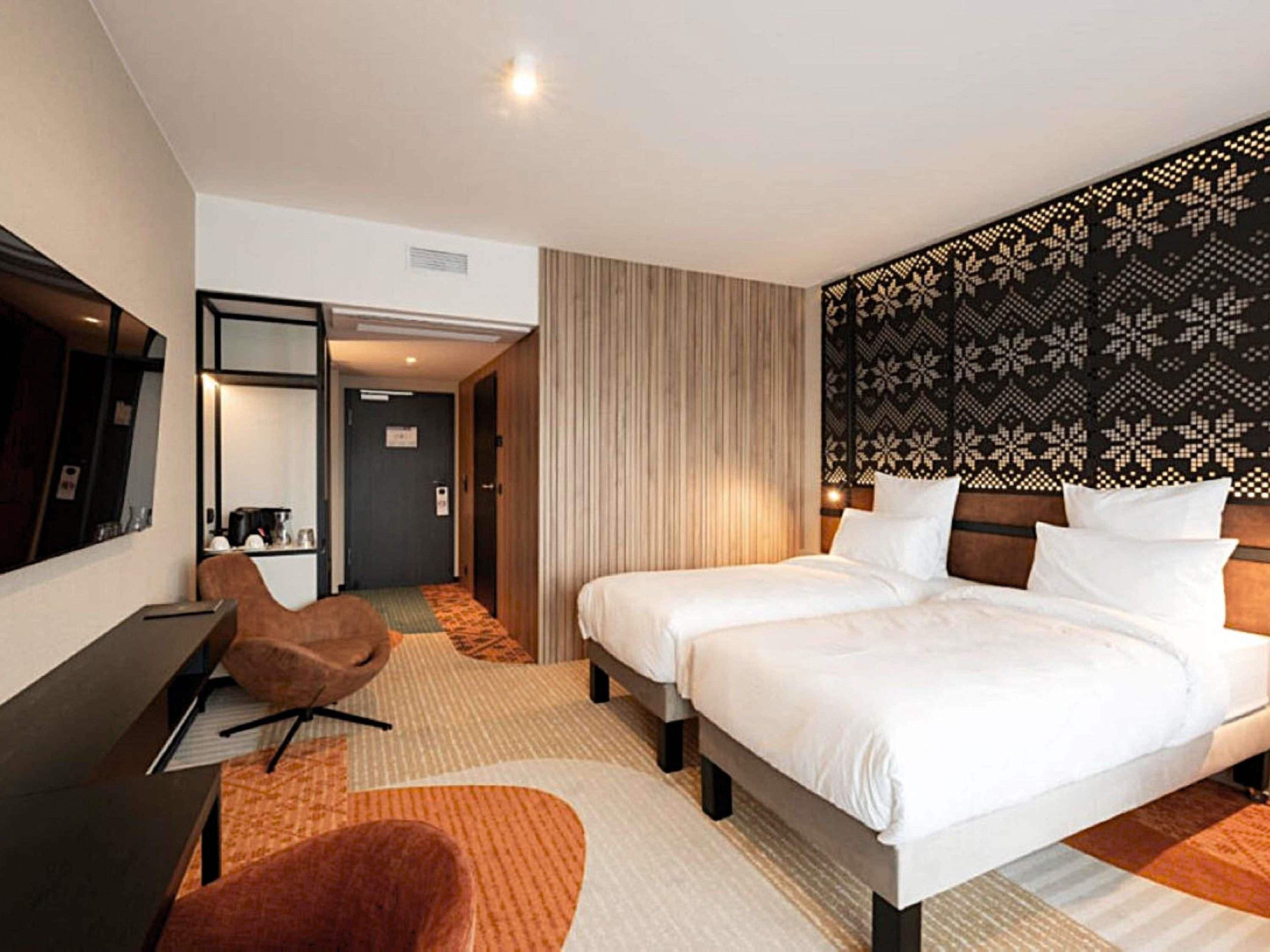 A hotel room with two beds, a desk, a chair, a mirror, and a patterned headboard.