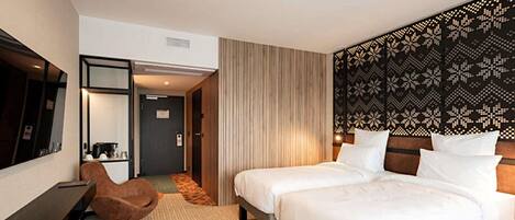 A hotel room with two beds, a desk, a chair, a mirror, and a patterned headboard.