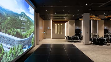 Un hall d’hôtel doté d’un grand écran diffusant des images de paysages, d’un comptoir d’accueil et d’un espace repas avec des tables préparées pour les clients.