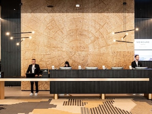 Uma receção com painel de parede em madeira, um ecrã digital a exibir 'Mercure Hotel' e um candelabro moderno.