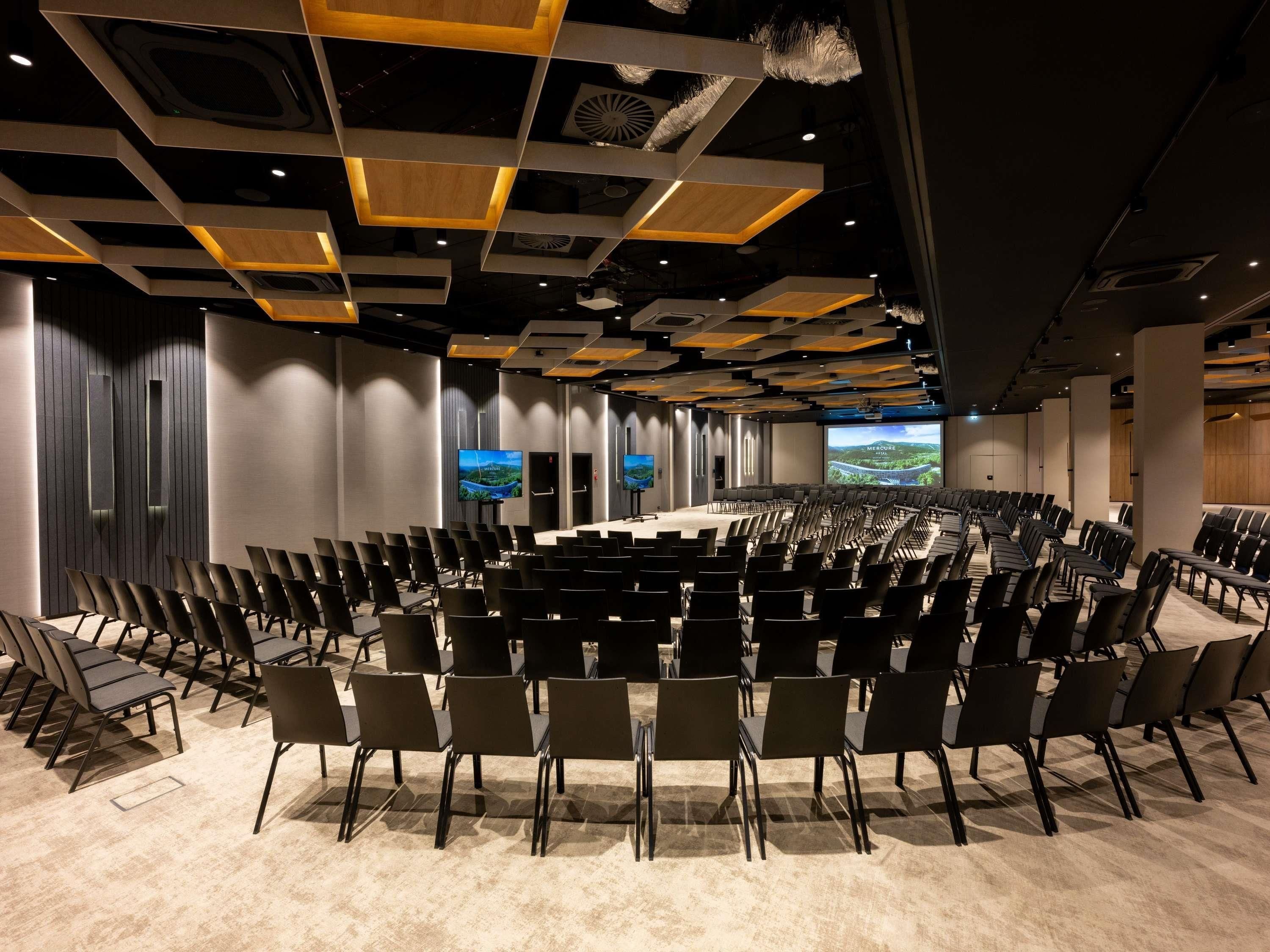 A conference room with rows of chairs, a stage, and multiple screens displaying landscapes.