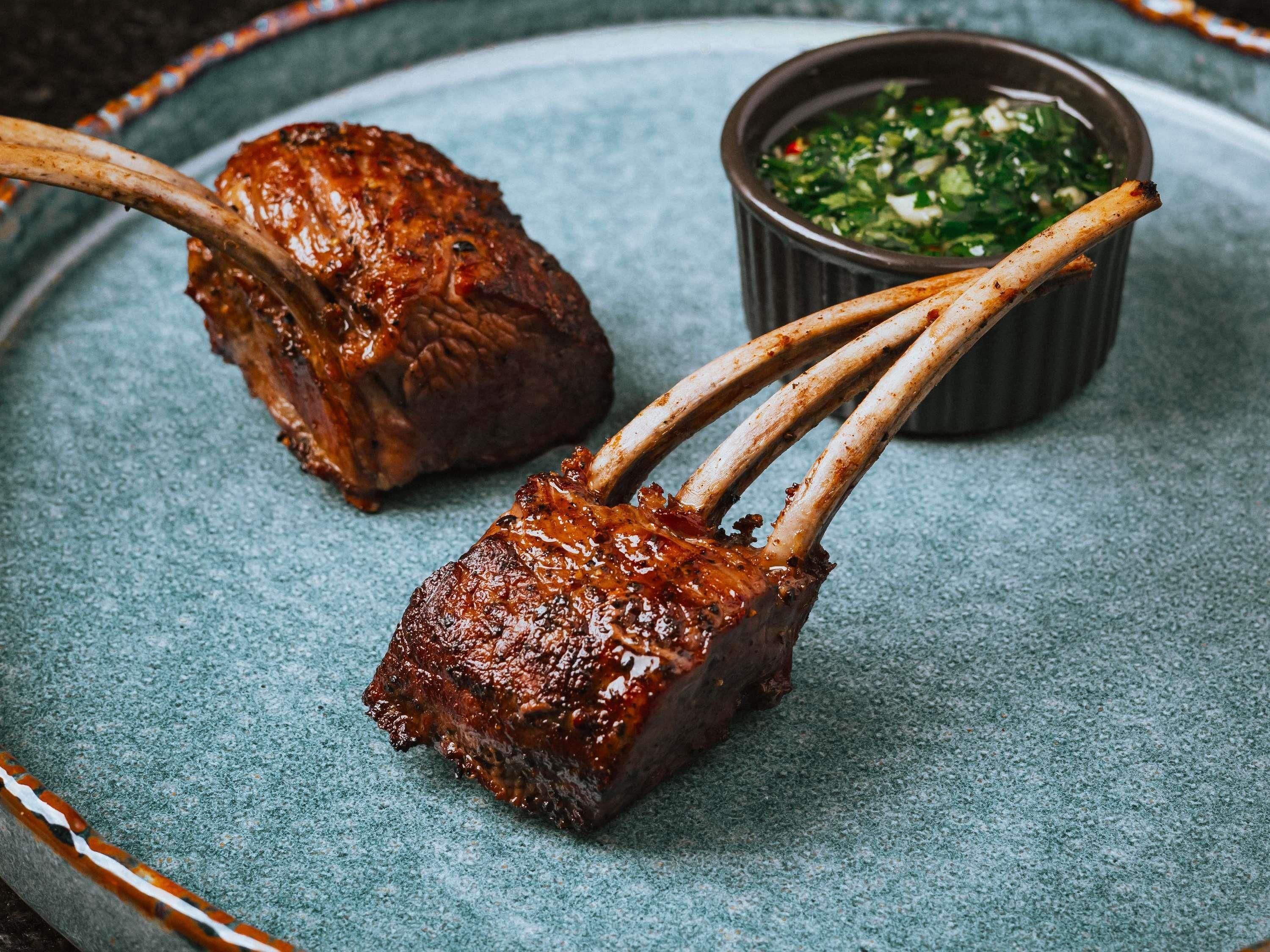 A plate with two grilled lamb chops and a bowl of green sauce.