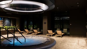 Un espace bien-être comprenant un jacuzzi, des chaises longues et un luminaire moderne au plafond.