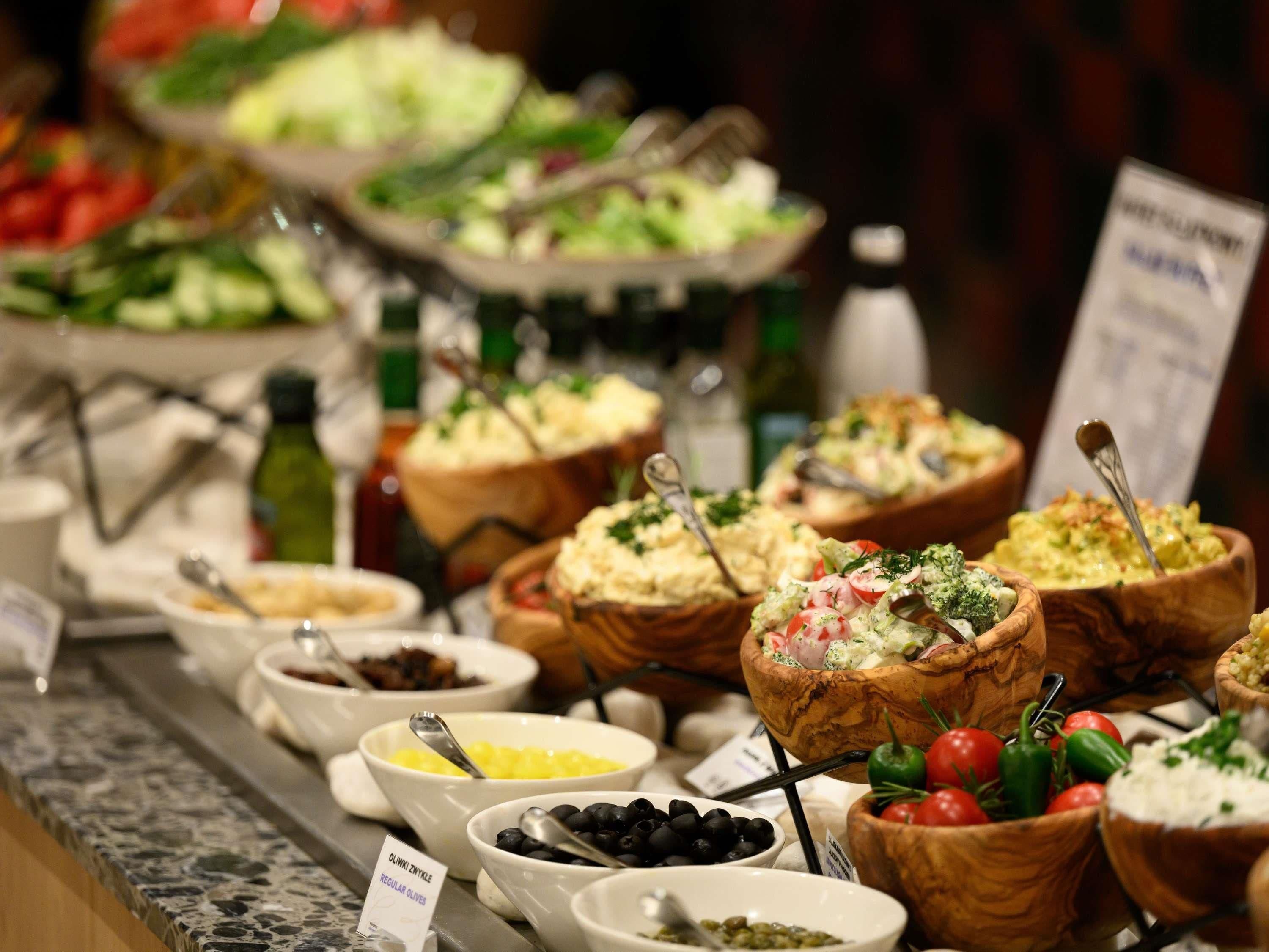A buffet with various dishes in bowls, including a sign for regular olives.