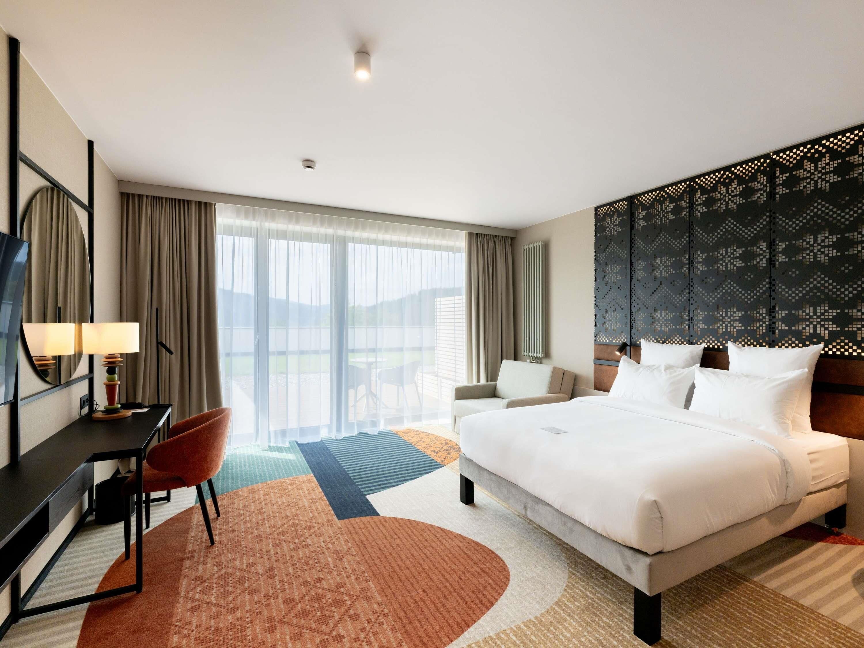 Hotelkamer met een groot bed, een bureau met stoel, een televisie en uitzicht op het omliggende landschap.