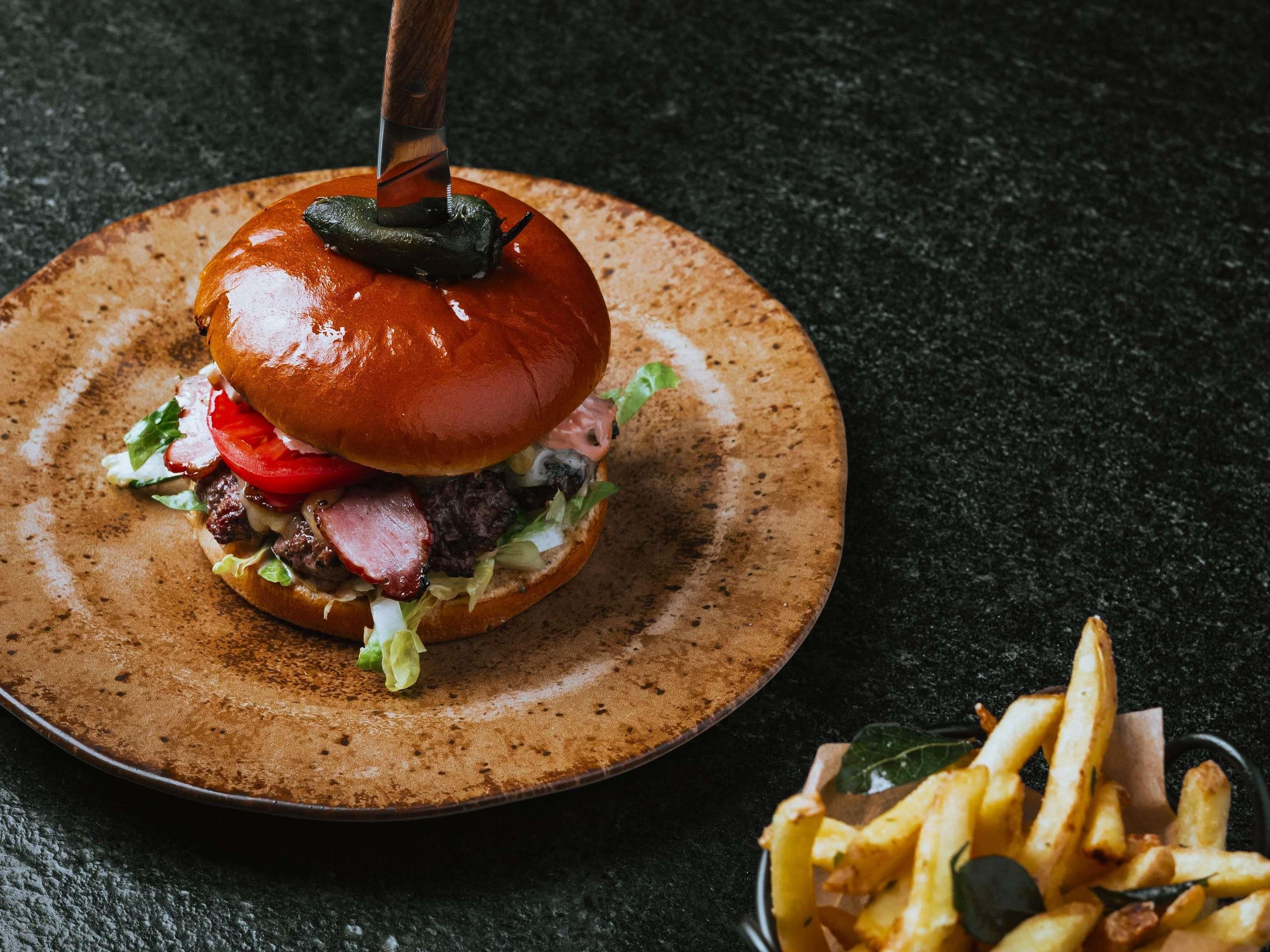 A burger with a pickled item on top, lettuce, tomato, and a bun, served on a plate with fries.