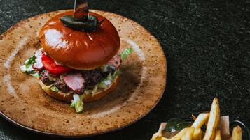A burger with a pickled item on top, lettuce, tomato, and a bun, served on a plate with fries.