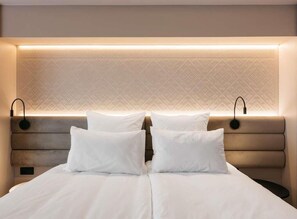 Une chambre d’hôtel comprenant un lit, deux tables de chevet et une tête de lit dotée d’un éclairage intégré.