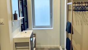 A modern bathroom with a white vanity, a mirror, a window, and a wooden drying rack. - Chez Fanf et Nanie (Isigny-sur-Mer)