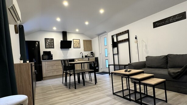 A modern living room with a sofa, a coffee table, and a dining area with chairs and a table. - Chez Fanf et Nanie (Isigny-sur-Mer)