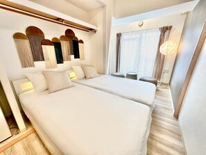 Habitació d'hotel amb dos llits, una zona de seients petita i un finestral gran amb cortines.