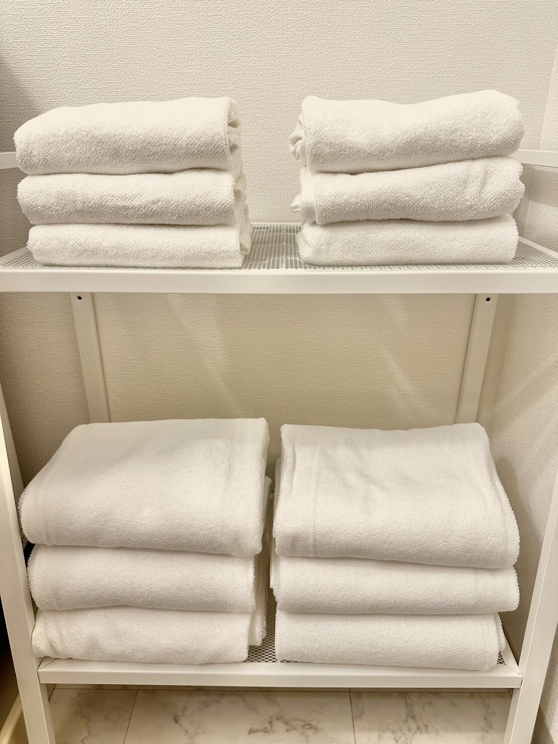 A white shelf with neatly folded white towels stacked in pairs.