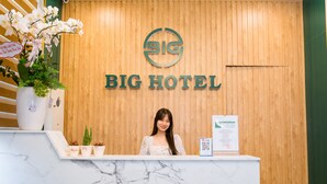 A reception desk with a wooden panel wall, a logo, and a sign that reads "BIG HOTEL". - BIG HOTEL (Hue)