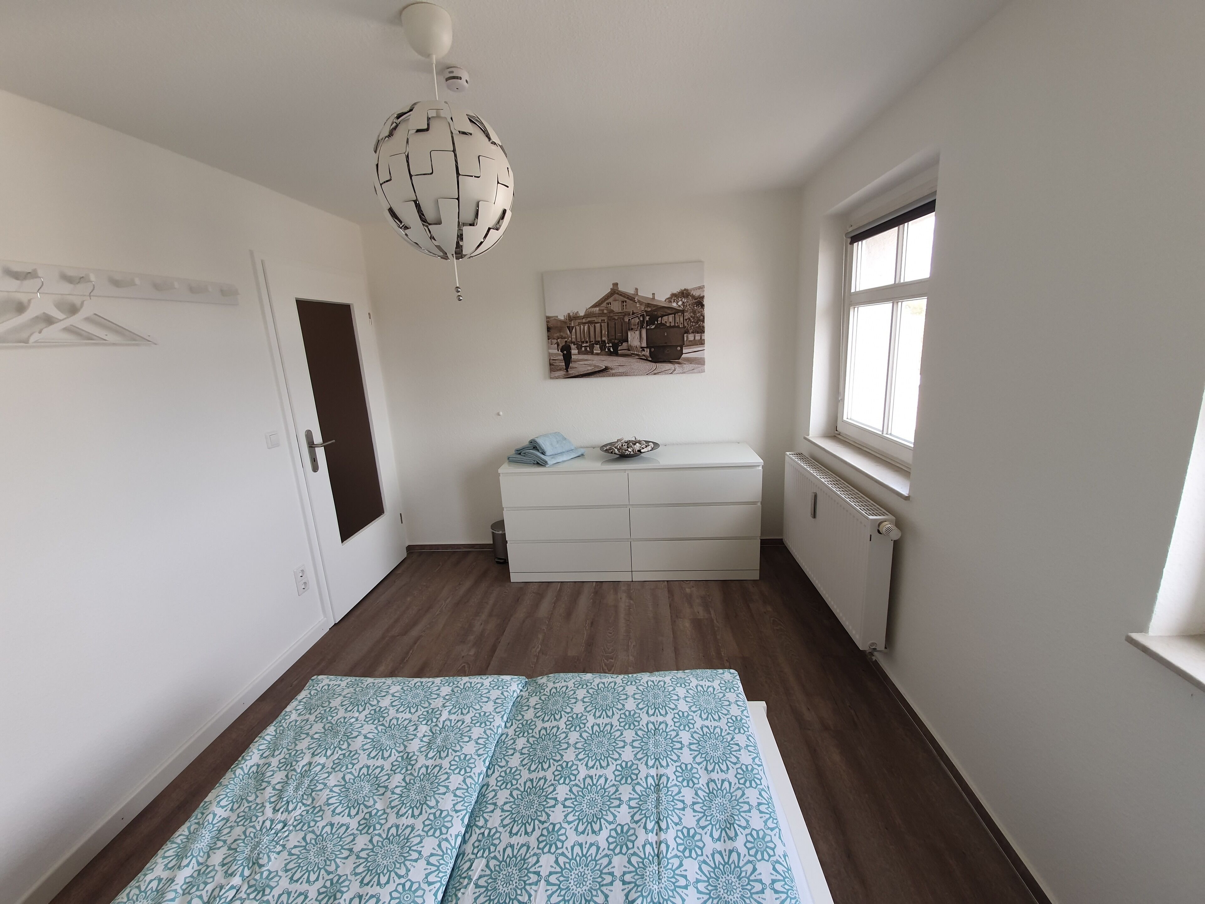 A bedroom with a bed, a dresser, a radiator, a window, and a globe light.