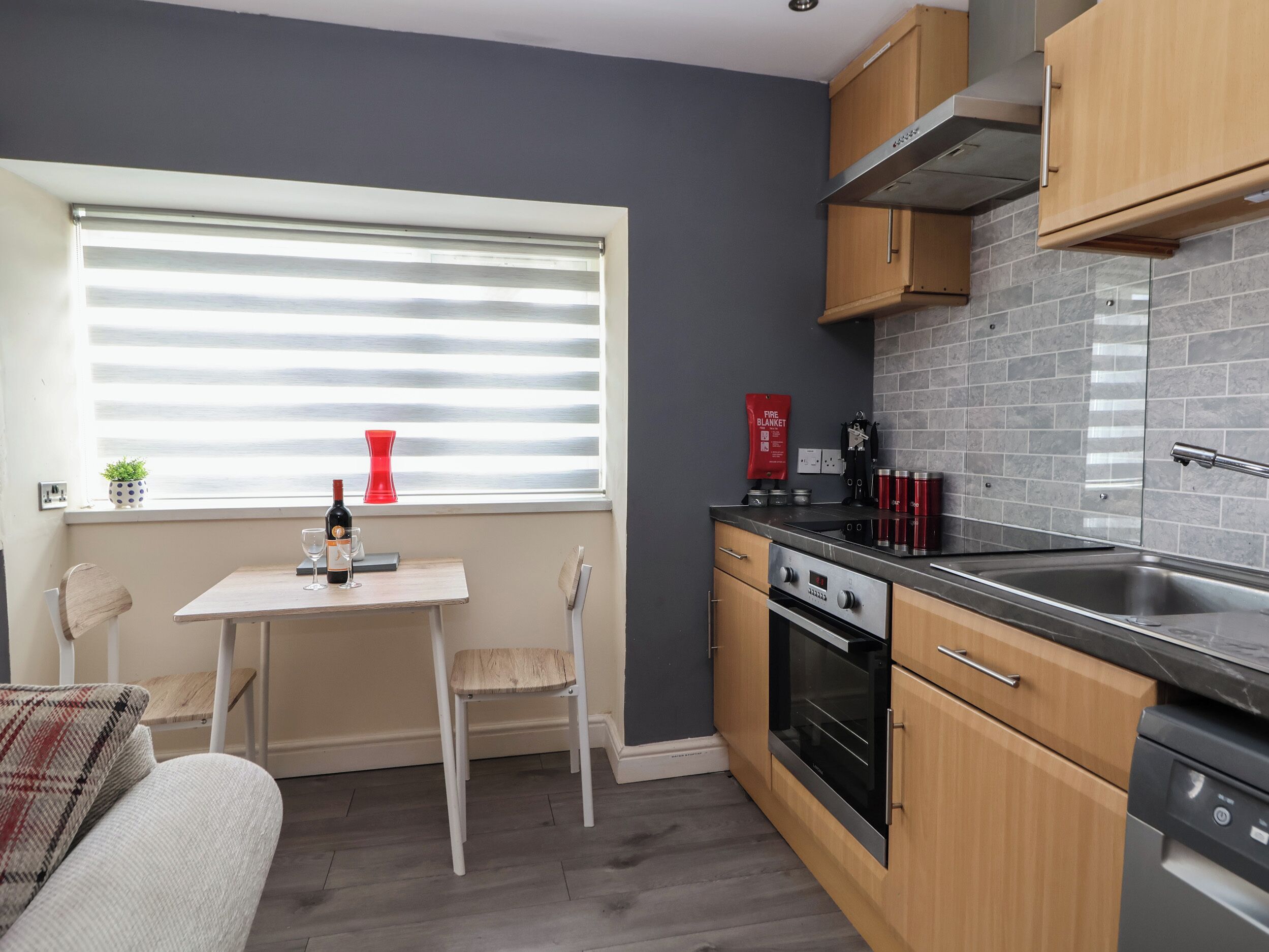 A modern kitchen with a dining area, featuring a window with blinds, a stove, and a sink.