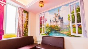 Een kamer met een groot muurdecoratie van een kasteel en een rivier, twee bruine banken, een kleine tafel en een raam met roze gordijnen.