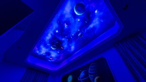 Een kamer met een sterrenhemelplafond en een ruimtevaartmuurdecoratie.