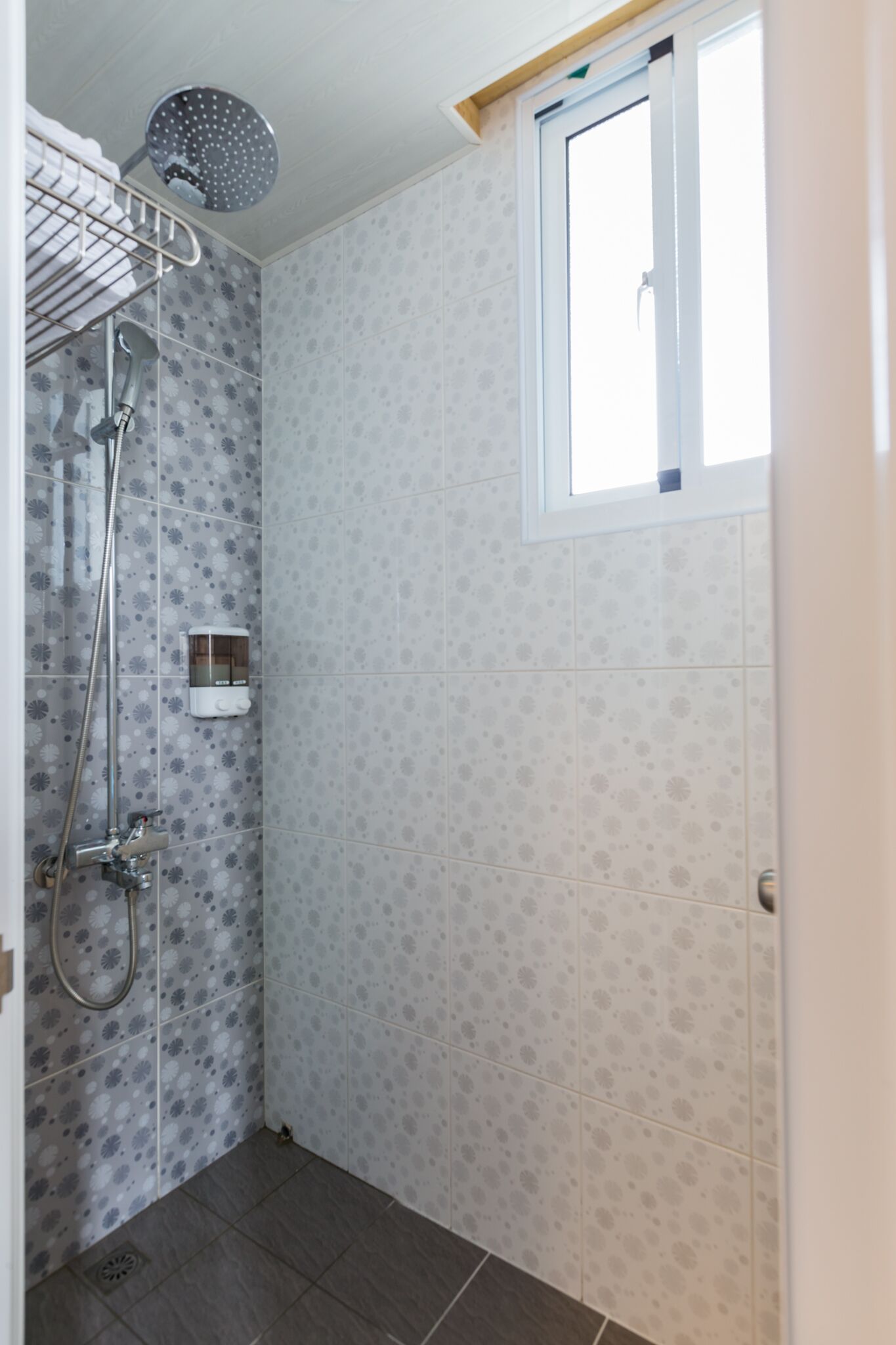 A small bathroom with a shower, a window, and patterned tiles.