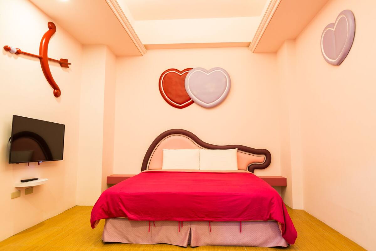 A bedroom with a bed, a TV, and heart-shaped decorations on the wall.