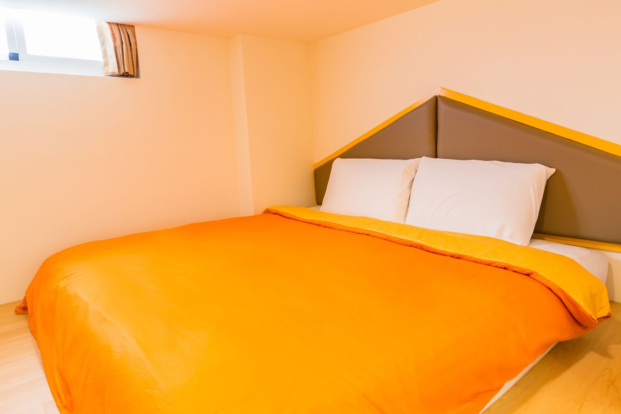 Una cama con colcha naranja y cabecera con detalle amarillo.