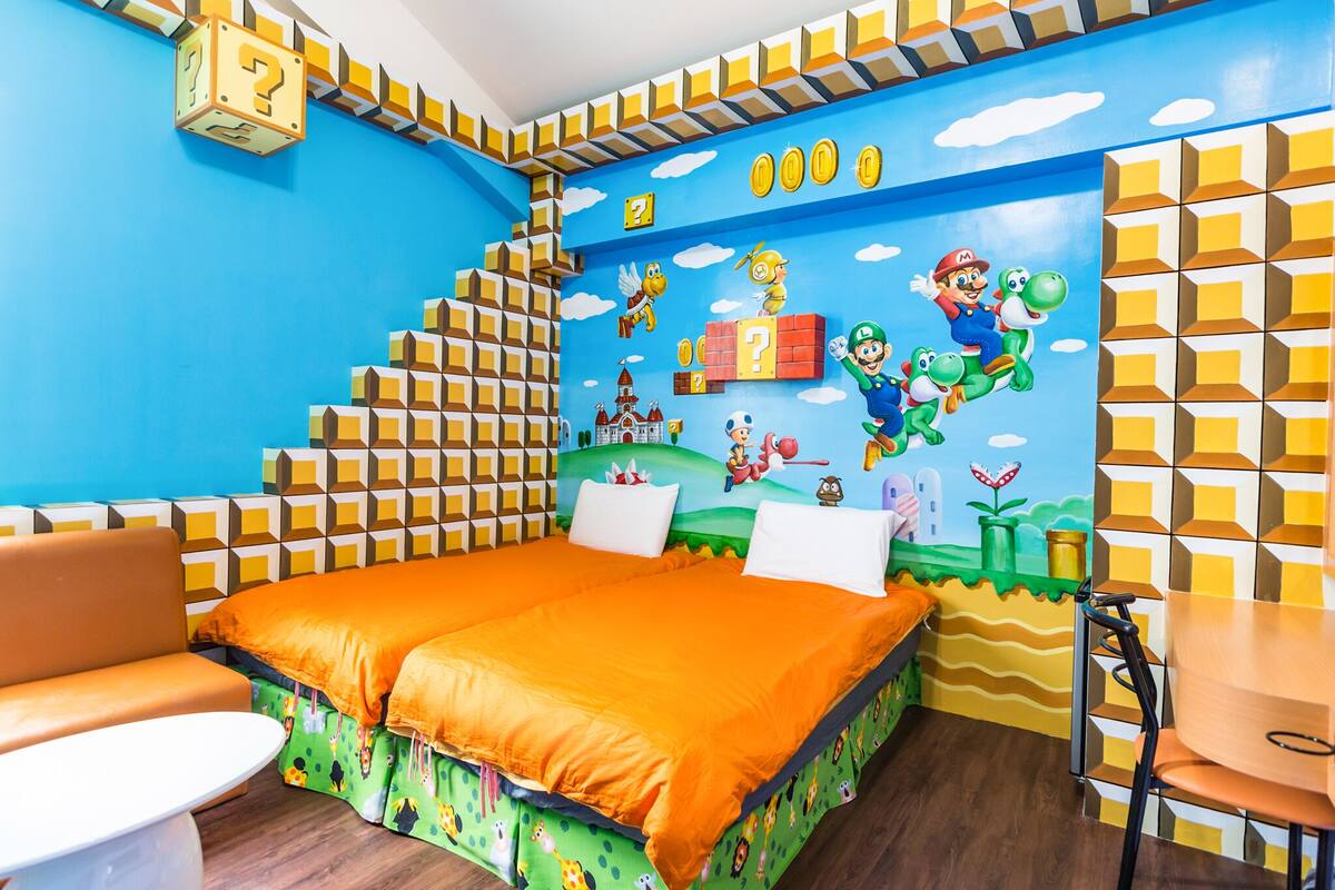 A room with a bed, two chairs, a small table, and a wall mural.