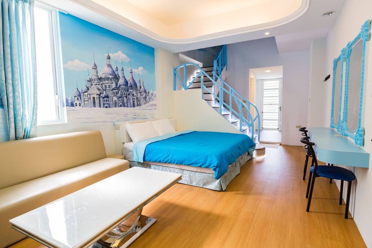 A modern room with a bed, a sofa, a dining table, and a staircase.