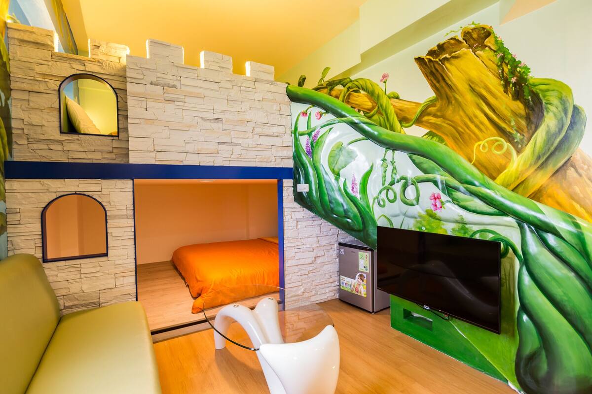 A room with a bunk bed, a flat-screen TV, a mirror, and a mural of a tree trunk.