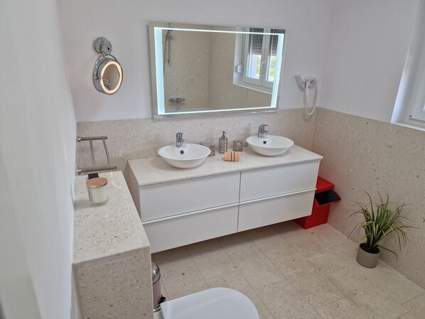 A modern bathroom with two sinks, a large mirror, and a potted plant.