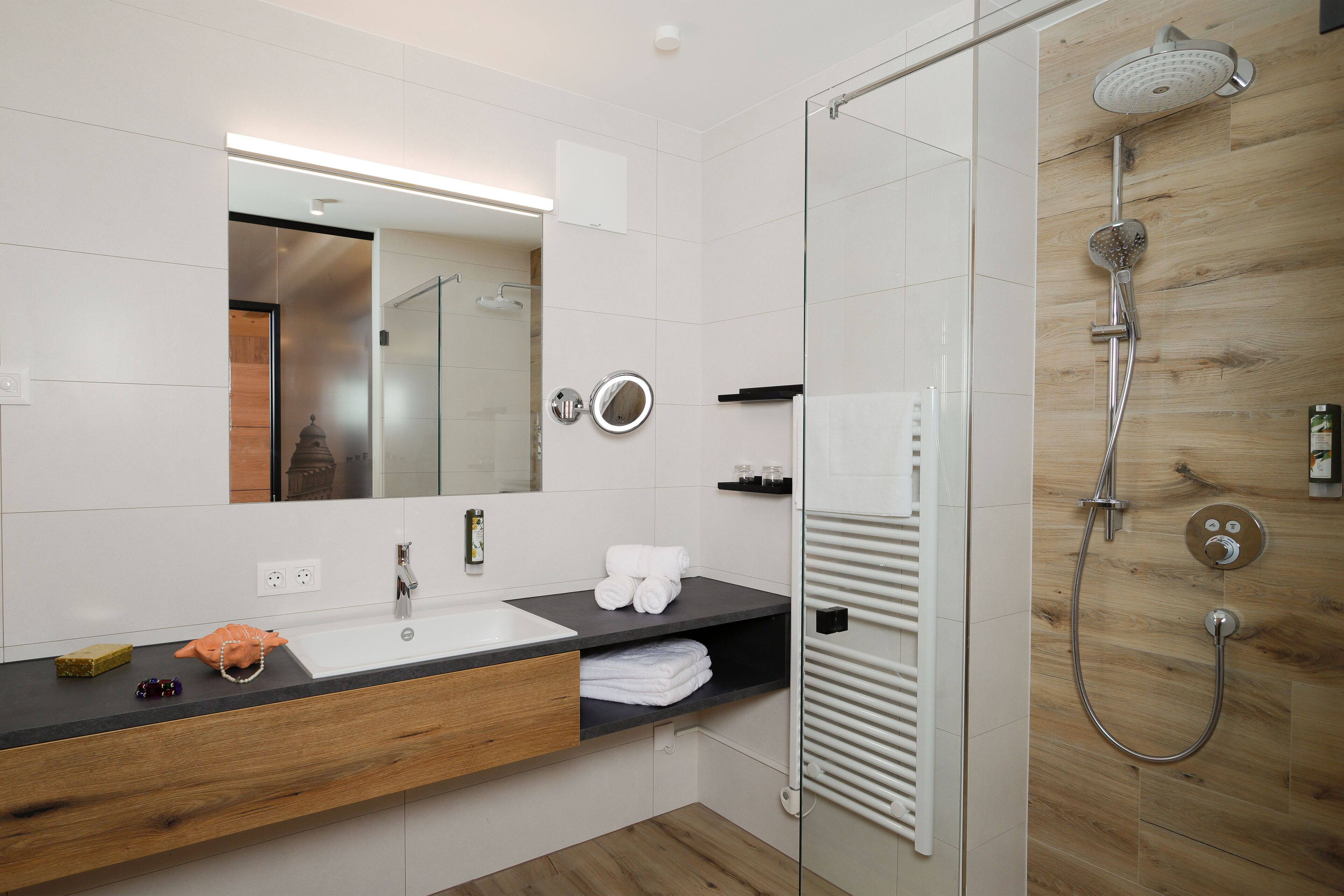 A modern bathroom with a wooden vanity, a large mirror, and a glass shower enclosure.