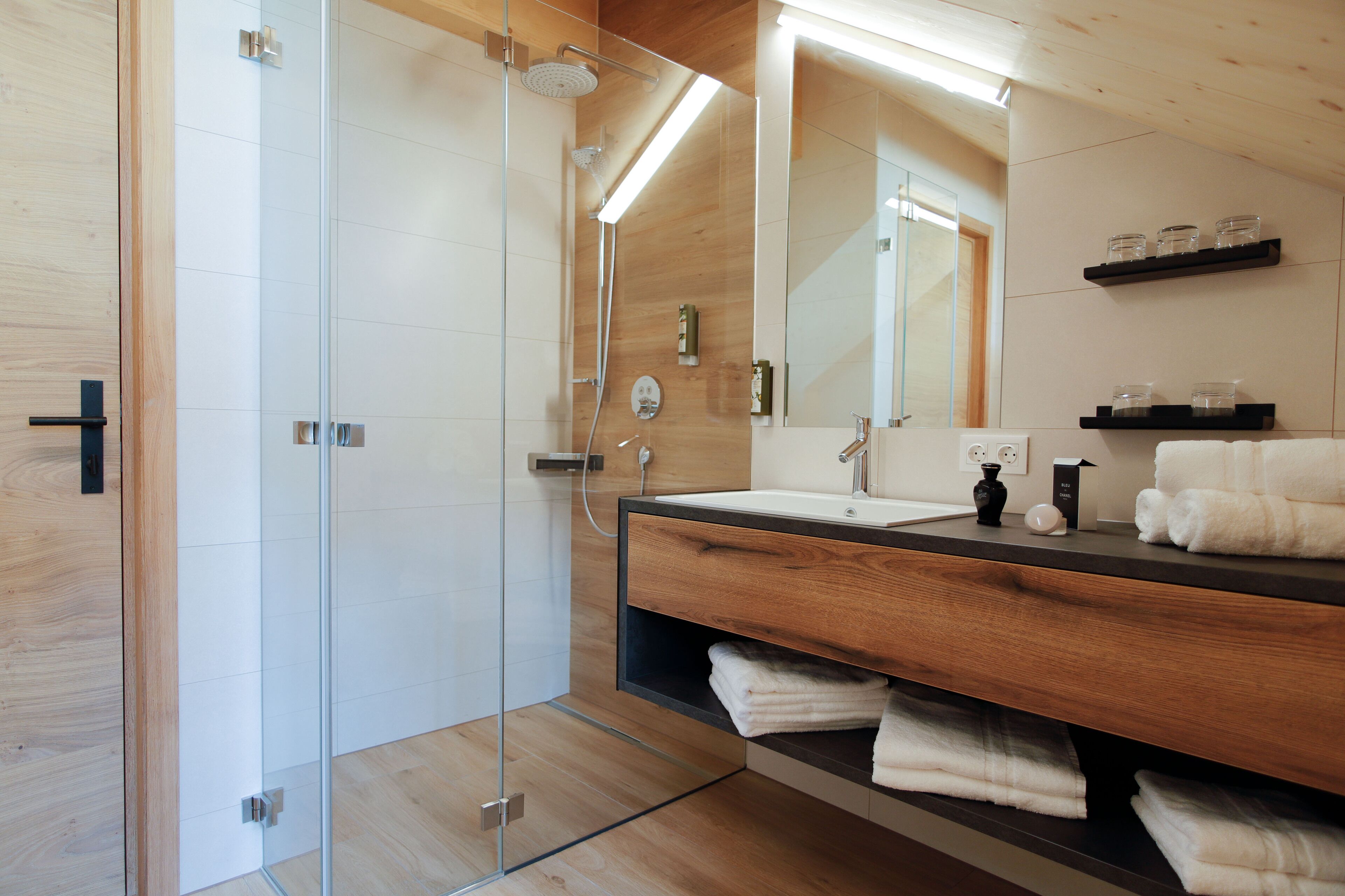Un baño moderno con cabina de ducha de vidrio, tocador de madera con lavamanos y un espejo grande.
