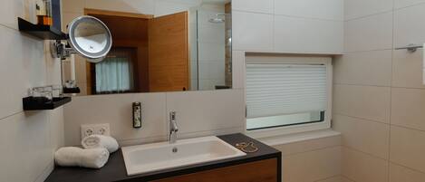 A modern bathroom with a wooden vanity, a white sink, a mirror, and a window with blinds.