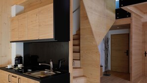 Uma cozinha moderna com armários de madeira e bancada preta, uma escada com guarda-corpo de vidro e vista para o exterior.