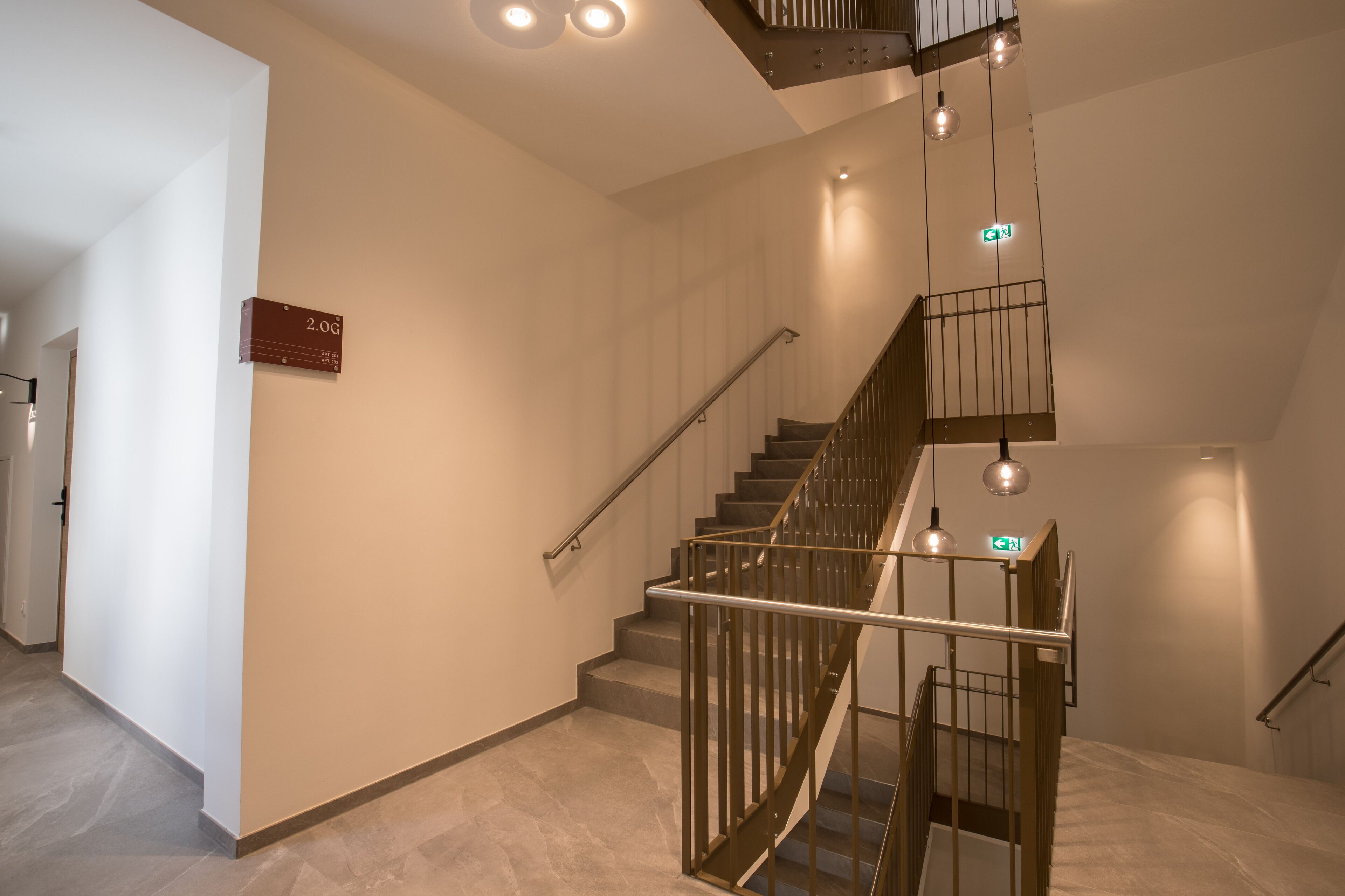 A modern interior with a staircase, metal railings, and pendant lighting.