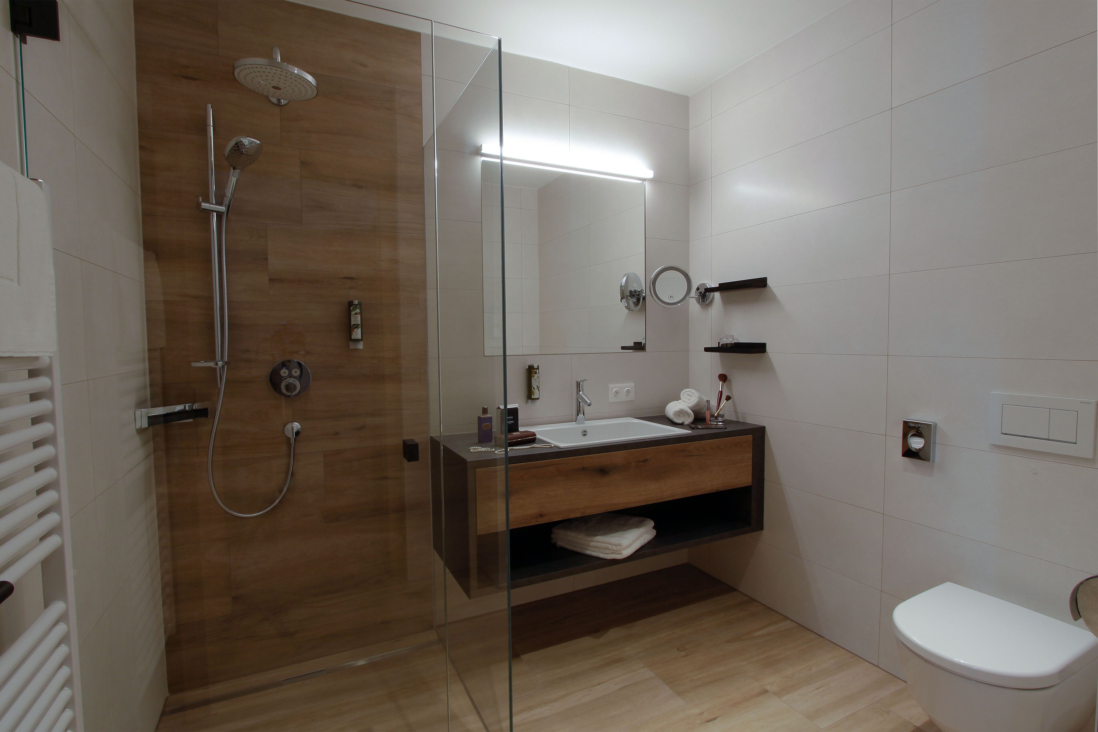 A modern bathroom with a glass-enclosed shower, a wooden vanity, a white sink, and a toilet.