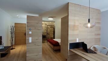 Una habitación moderna con suelo de madera, una cama con una colcha roja, un escritorio con un ordenador portátil y una lámpara colgante.
