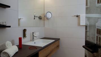 Une salle de bain avec un lavabo blanc, un miroir, une serviette et une bouteille rouge.