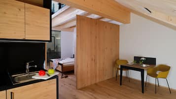 A compact kitchen with a sink, a dining area with a table and chairs, and a bedroom with a bed and a window.