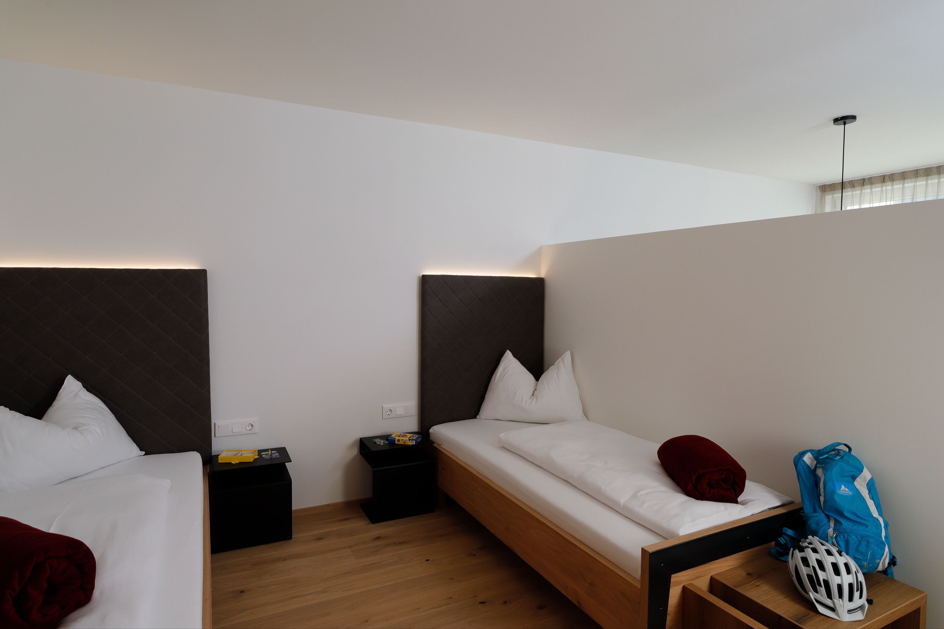 Ein modernes Hotelzimmer mit zwei Einzelbetten, einem kleinen Nachttisch, einer Nachttischlampe und einer Holzbank.