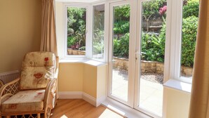 A corner room with a wicker chair, a bay window, and a view of a garden.